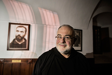 Padre Luciano Lotti accanto a una fotograia di Padre Pio giovane nel refettorio antico di San Giovanni Rotondo.